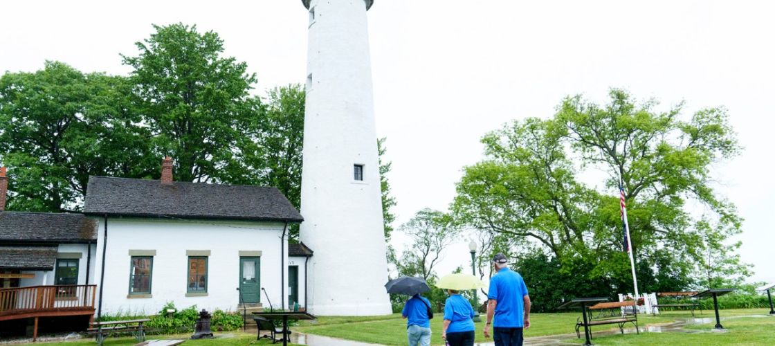 Two people walk toward a lighthouse