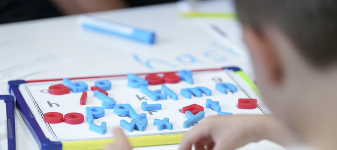 A view of a child from the back.  The student is participating in an activity that focuses on practicing letters. 