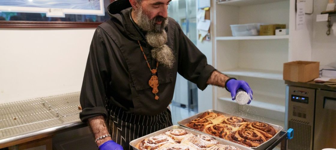 A man sprinkles powdered sugar over panfuls of pastries