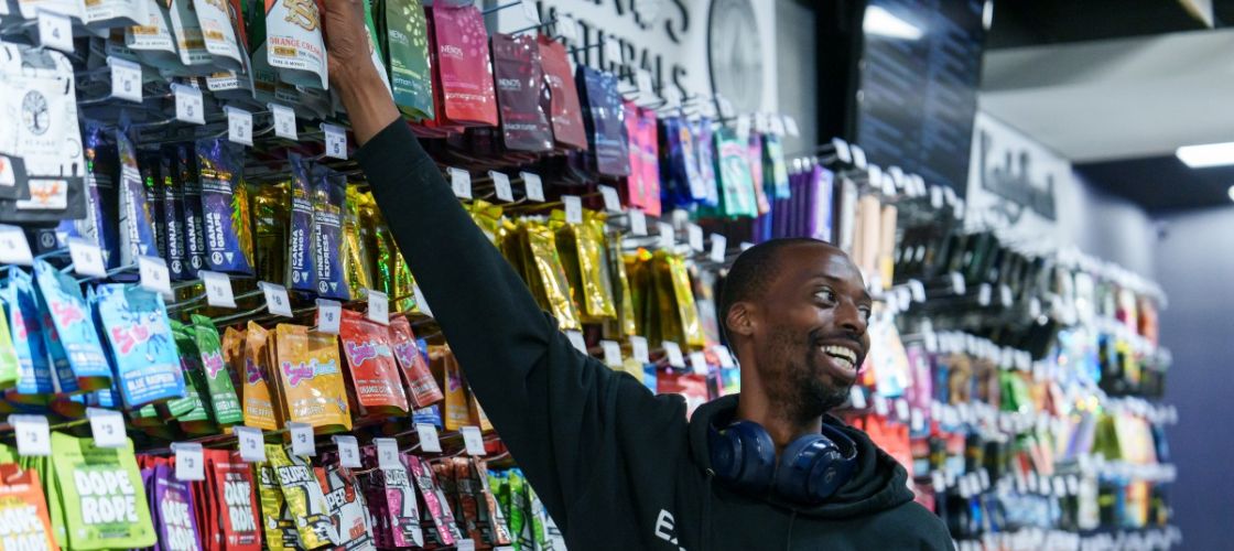 A man reaches up to grab a product from a wall full of marijuana products
